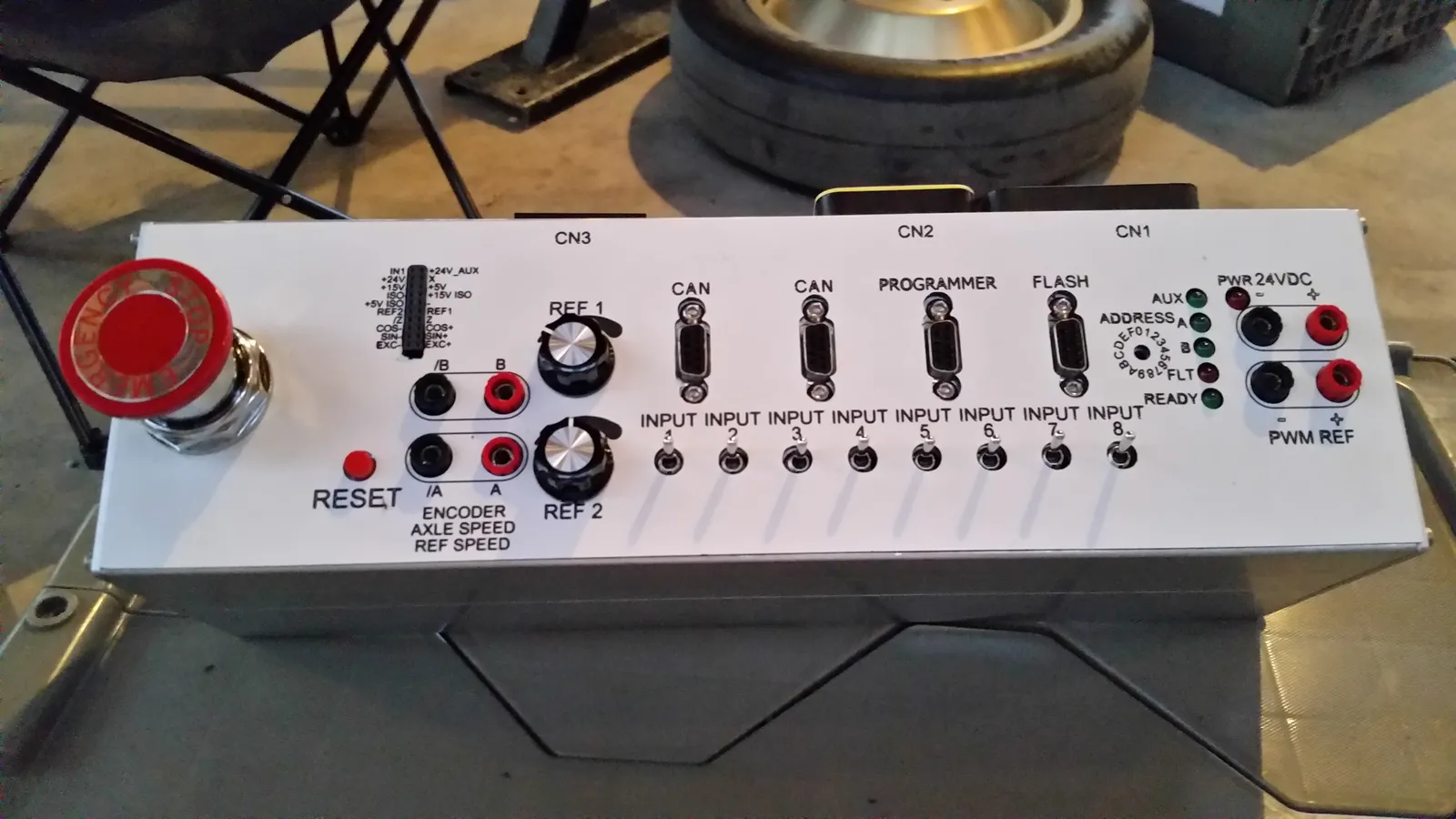 The test station control box with communication ports, knobs, an emergency stop, and encoder inputs